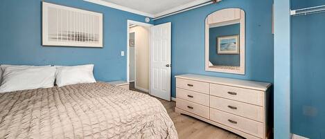 Une chambre à coucher comprenant un lit, une commode, une porte et un miroir fixé au mur.