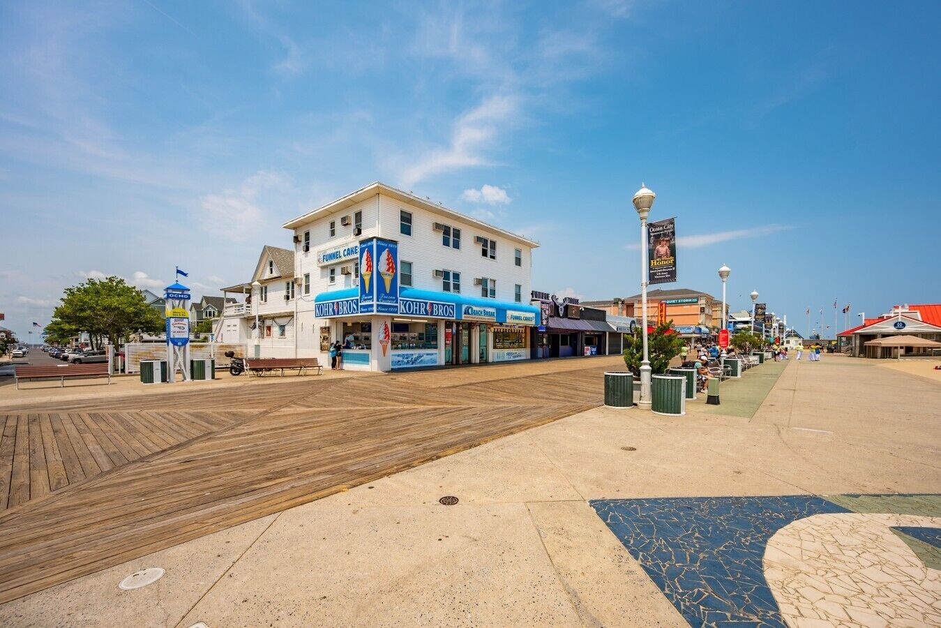 A boardwalk with shops, including a funnel cake stand, and a clear blue sky.