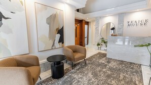 Una zona de recepción con mostrador de mármol, dos sillones marrones y arte abstracto en las paredes.