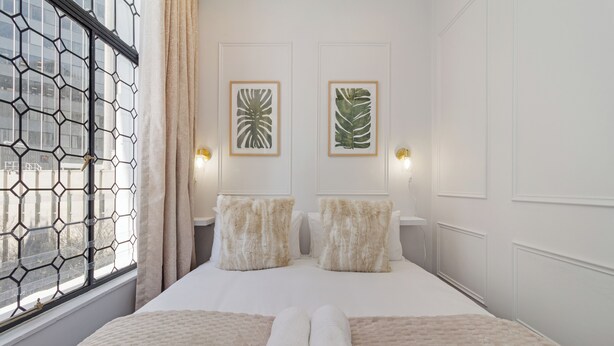 Habitación de hotel con una cama grande, dos lámparas fijadas a la pared y dos obras de arte con hojas enmarcadas.