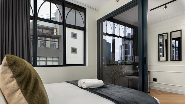A modern hotel room with a large bed, a view through a glass door, and a cityscape outside.