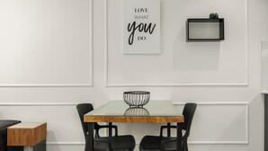 A dining area with a wooden table, black chairs, a glass-top table, and a wall-mounted sign.