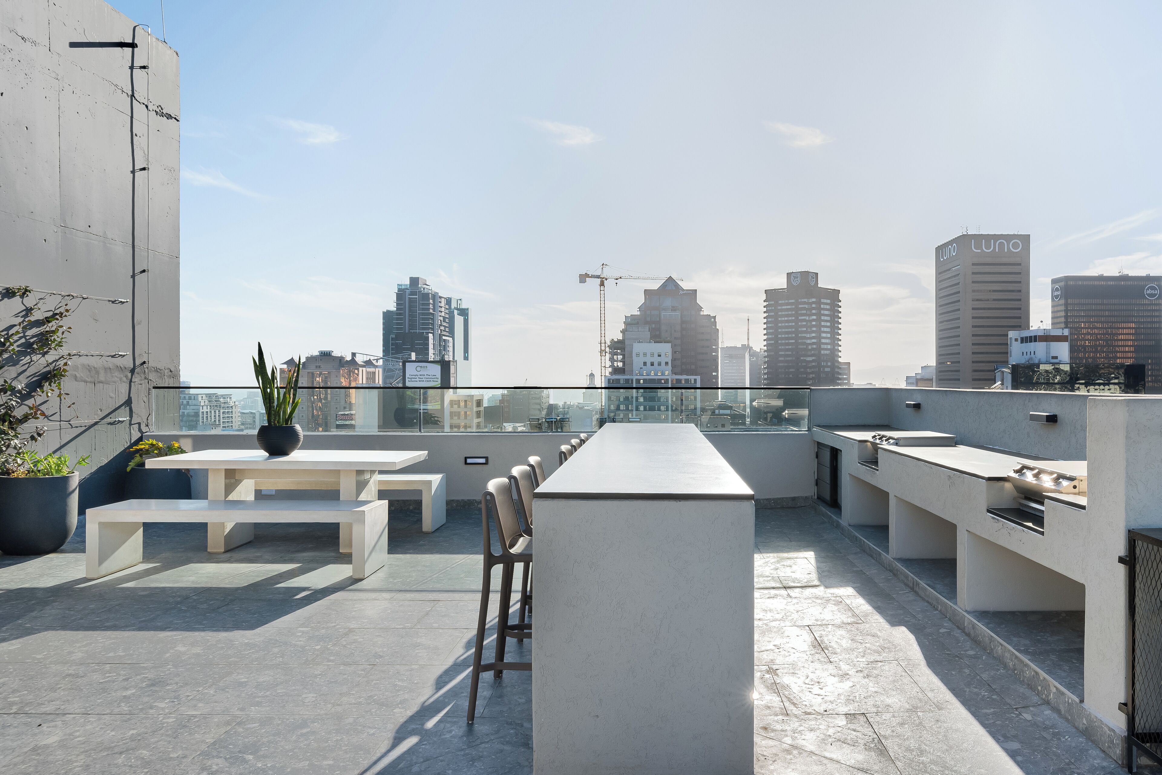 A rooftop terrace with a long table, benches, and a bar area.