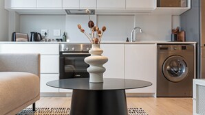 Cozinha moderna com ilha central, máquina de lavar roupa e área de refeições com sofá.