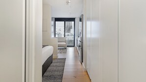 Um corredor estreito que leva a um quarto com uma cama, um sofá e uma área de cozinha com geladeira e fogão.