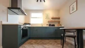 A compact kitchen with a herringbone floor pattern, a central island, and a dining area with a chair. - Modern Southville Escape | City & Harbourside (Bristol)