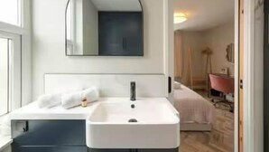 Een moderne badkamer met een witte wasbak, een spiegel en een deur naar een andere kamer.