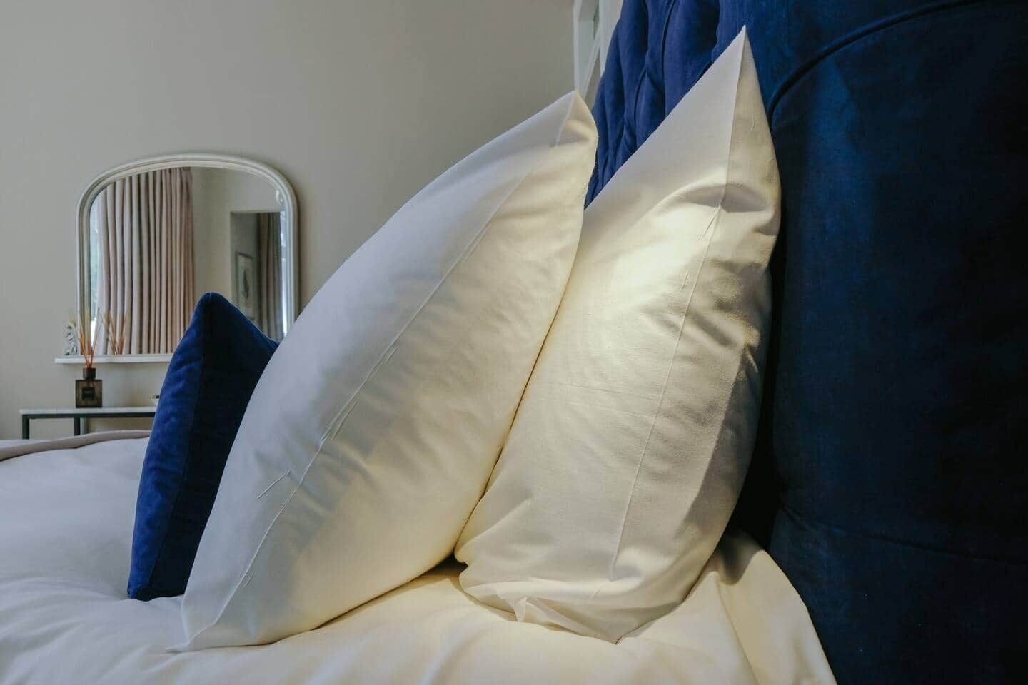 A bed with white and blue bedding, a mirror, and a small table with a vase.