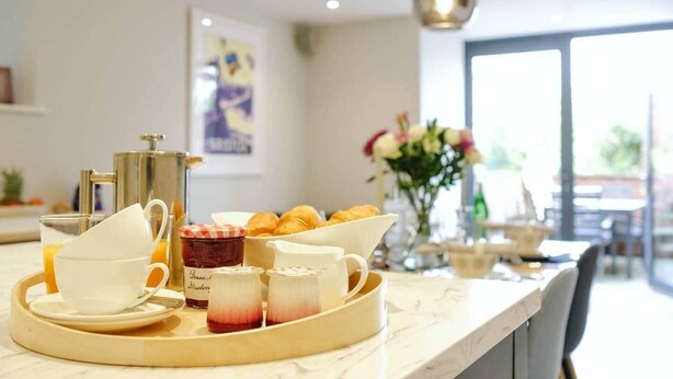 Ein Frühstücksbrett mit Croissants, einer Kaffeekanne und einem Krug Erdbeermarmelade.