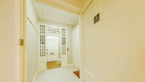 A narrow hallway with white walls and doors, a number sign on one wall, and a patterned floor. - Victorian Charm in Cotham | Free Parking (Bristol)