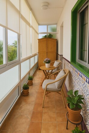 A balcony with a view of greenery, a wooden cabinet, two wicker chairs, a small round table, and potted plants. - Traditional Townhouse in Quiet Area with Patio and Lots of Natural Light (San Miguel)