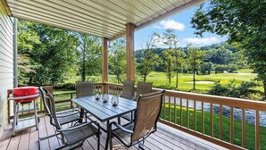 Una terraza techada al aire libre con una mesa y sillas, con vista a un campo de golf y una masa de agua.