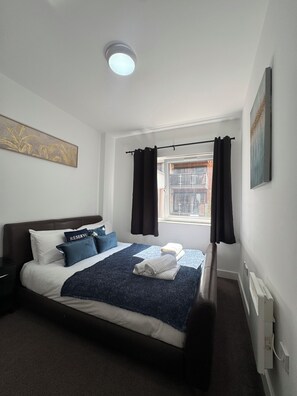 Quarto moderno com cama, mesa de cabeceira, janela com cortinas e luminária no teto.