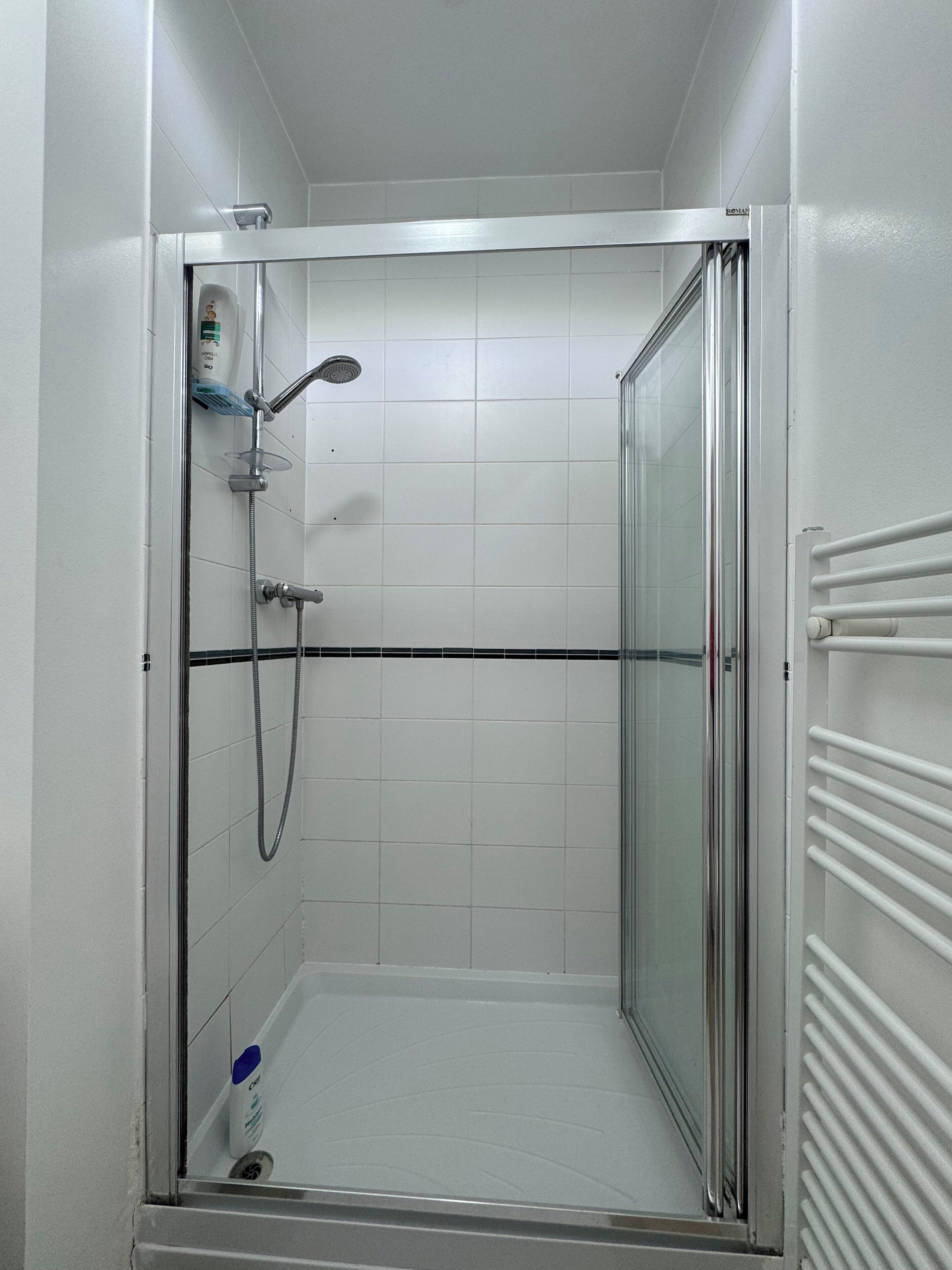 A small, enclosed shower area with a glass door, white tiled walls, and a white towel rack on the right.
