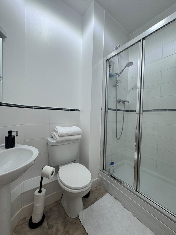 Uma casa de banho moderna com cabine de duche em vidro, lavatório branco e sanita.