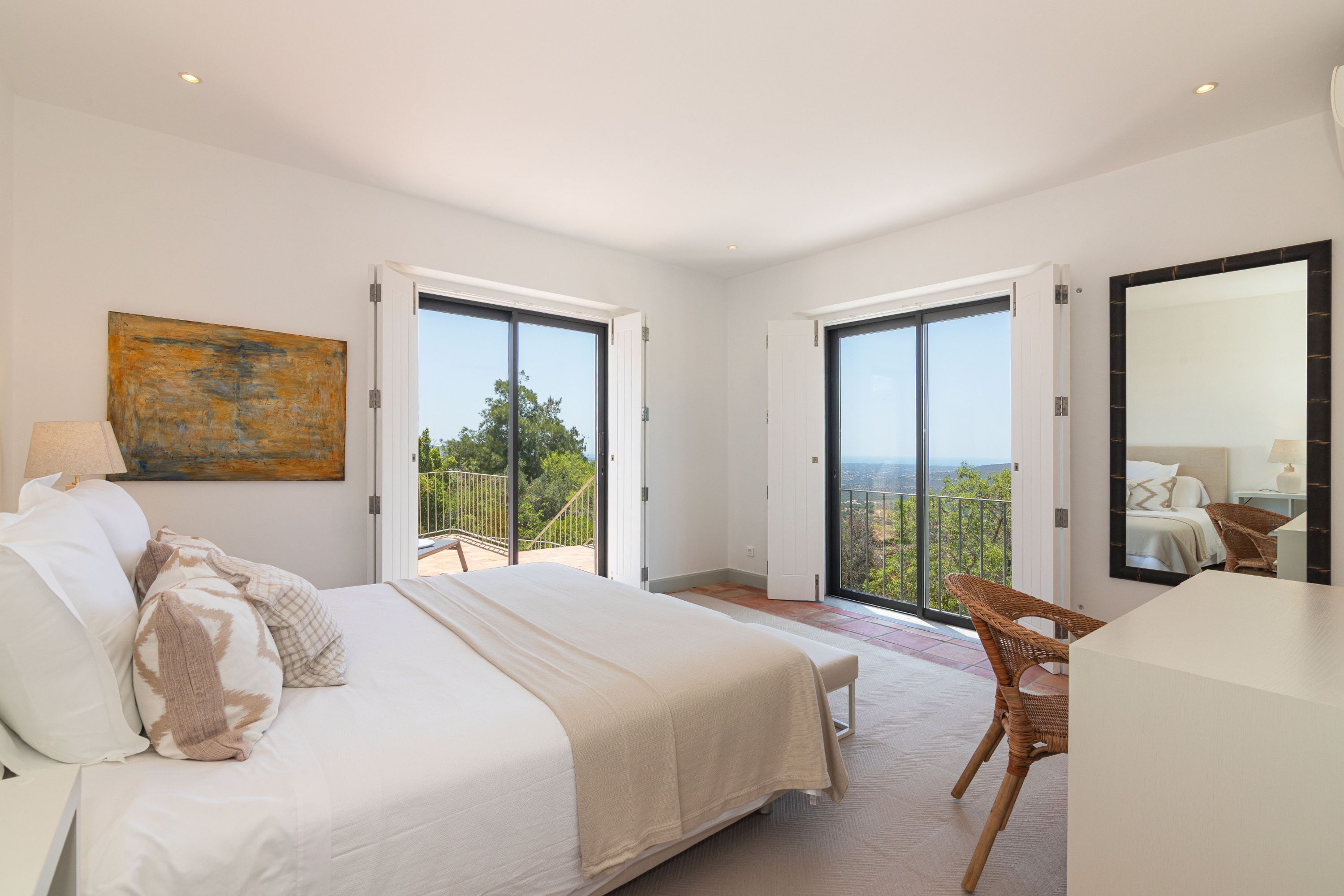 A bedroom with a large bed, a chair, and a balcony with a view.