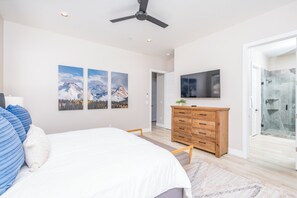 Une chambre à coucher comprenant un lit, une commode en bois, un téléviseur à écran plat et une douche en verre.