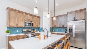 A modern kitchen with wooden cabinets, stainless steel appliances, and a central island with bar stools. - Super clean 3-bedroom townhome- Purgatory - Hot Tub/Views/Arcade Game/Firepit (Durango)