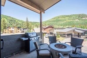 Un balcon avec un barbecue, des chaises en osier, une table ronde et une vue imprenable sur les montagnes.