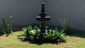 A stone fountain surrounded by ferns and cacti, set against a brick wall. - Free RV parking, two car garage, fenced backyard, minutes to Westgate (Glendale)