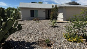 A single-story building with a garage, a small front yard with rocks and cacti, and a clear blue sky. - Free RV parking, two car garage, fenced backyard, minutes to Westgate (Glendale)