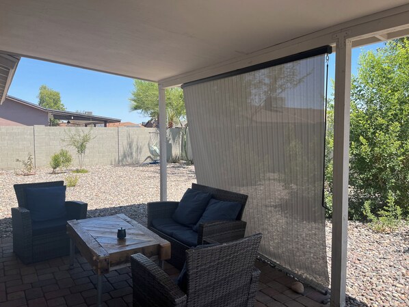 A covered patio area with wicker furniture, a table, and a view of a backyard.