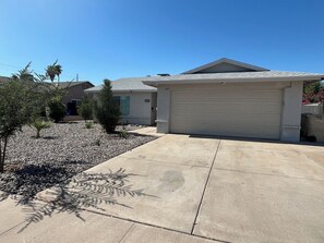 A residential property with a garage, a driveway, and a landscaped garden with small trees and shrubs.