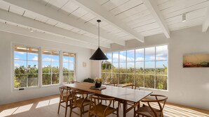 A spacious dining area with a long wooden table and chairs, large windows offering a view of the outdoors, and a black pendant light hanging above. - Gorgeous Newly Renovated Luxury Home Located 1 mile to Plaza Avail May 23- Aug 7 (Santa Fe)