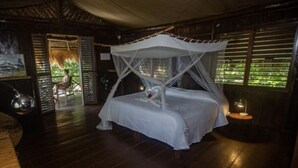 Una habitación con cama a dosel, una pequeña mesa con lámpara y vistas a la vegetación.