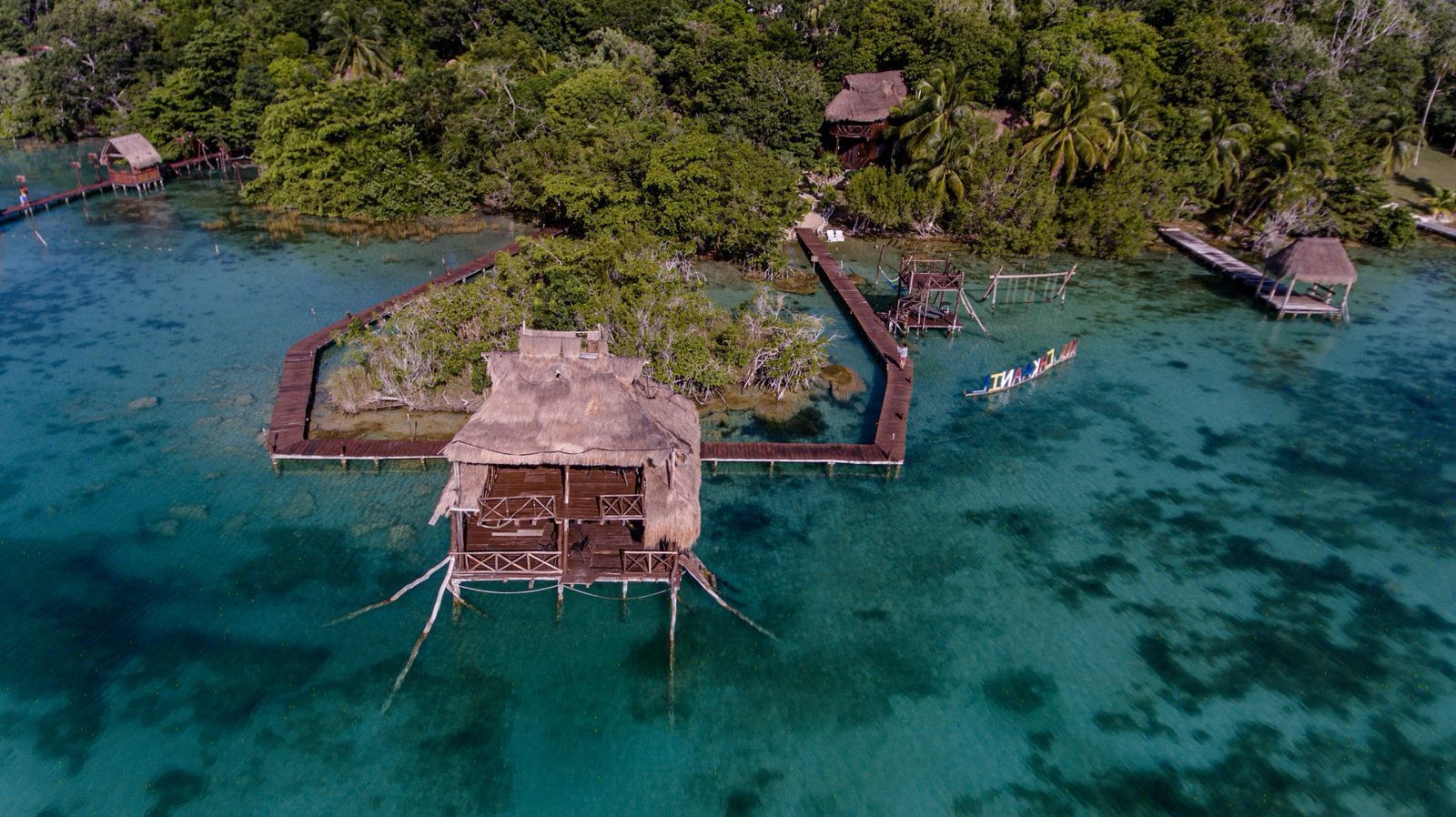 An aerial view of a tropical island with overwater bungalows connected by walkways.