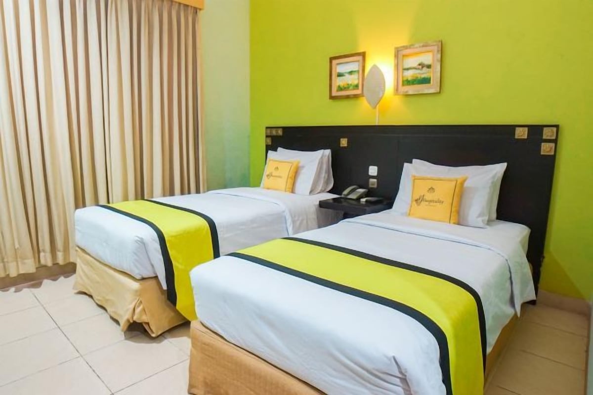 A hotel room with two beds, each with a white and yellow bedspread, a black headboard, and a bedside table with a lamp.