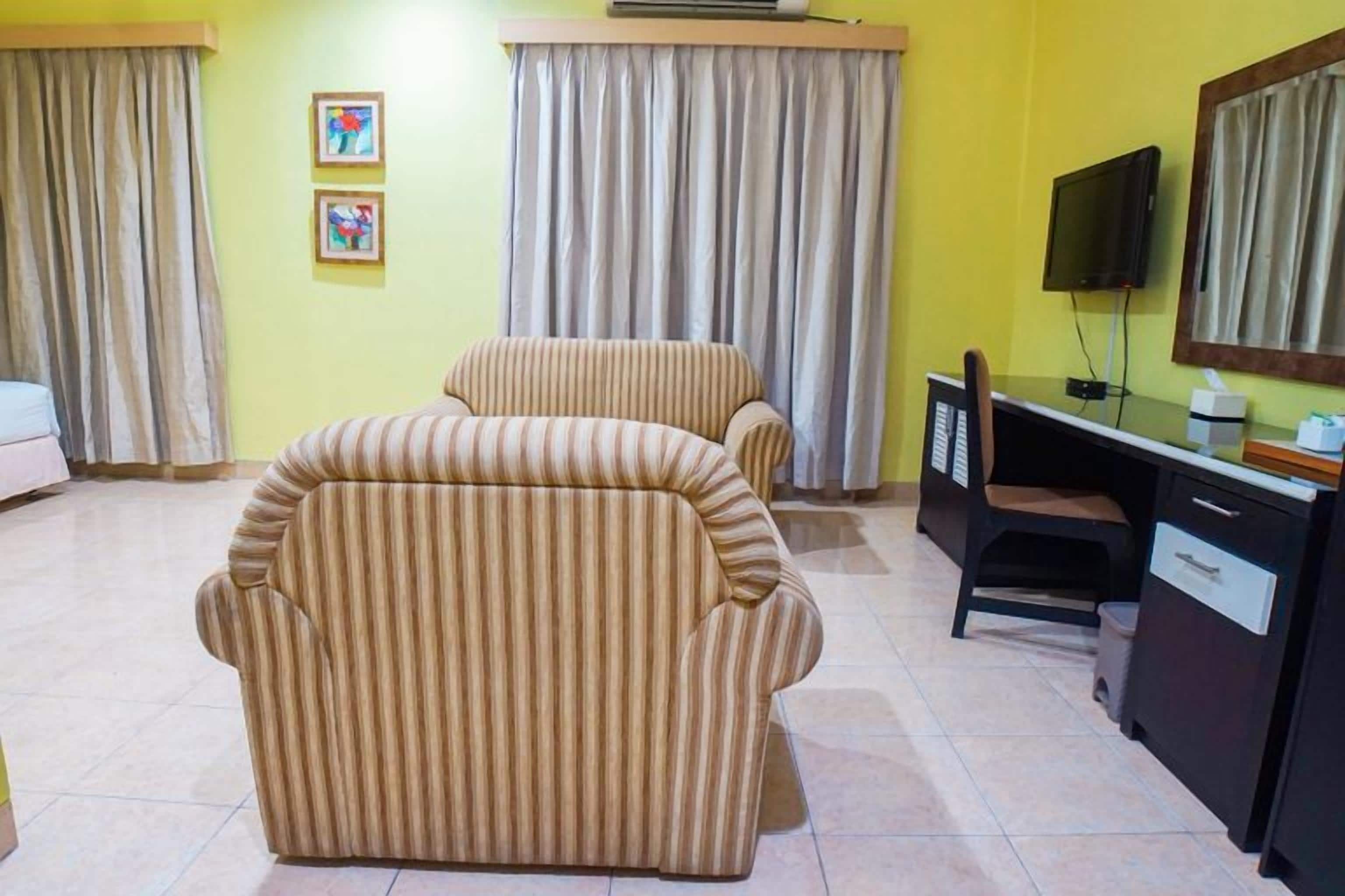 A room with a sofa, a desk with a chair, a television, and curtains.
