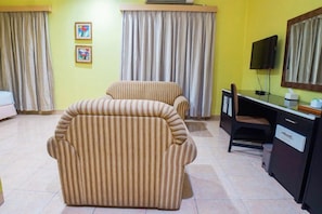 A room with a sofa, a desk with a chair, a television, and curtains. - Hotel Bumi Siliwangi by My Hospitality (Sukasari)