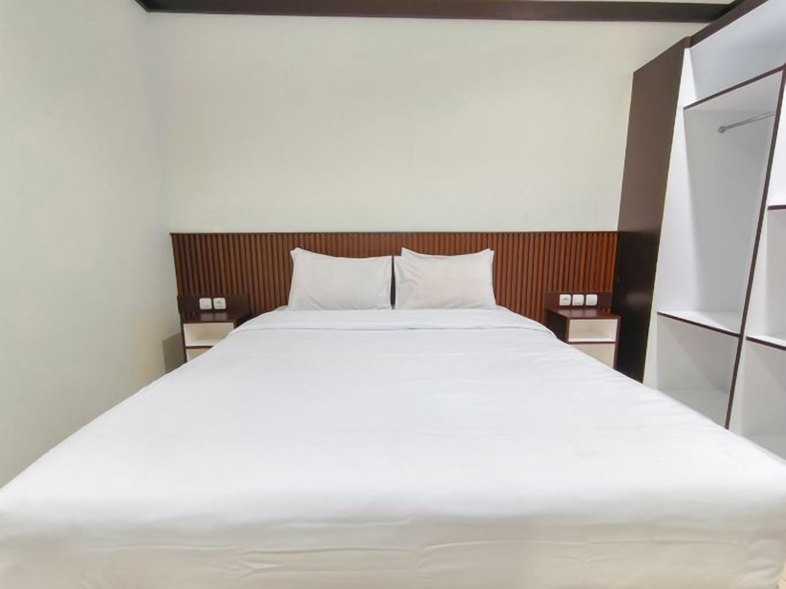 A hotel room with a large bed, wooden headboard, two bedside tables, and a wardrobe.