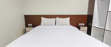 A hotel room with a large bed, wooden headboard, two bedside tables, and a wardrobe.