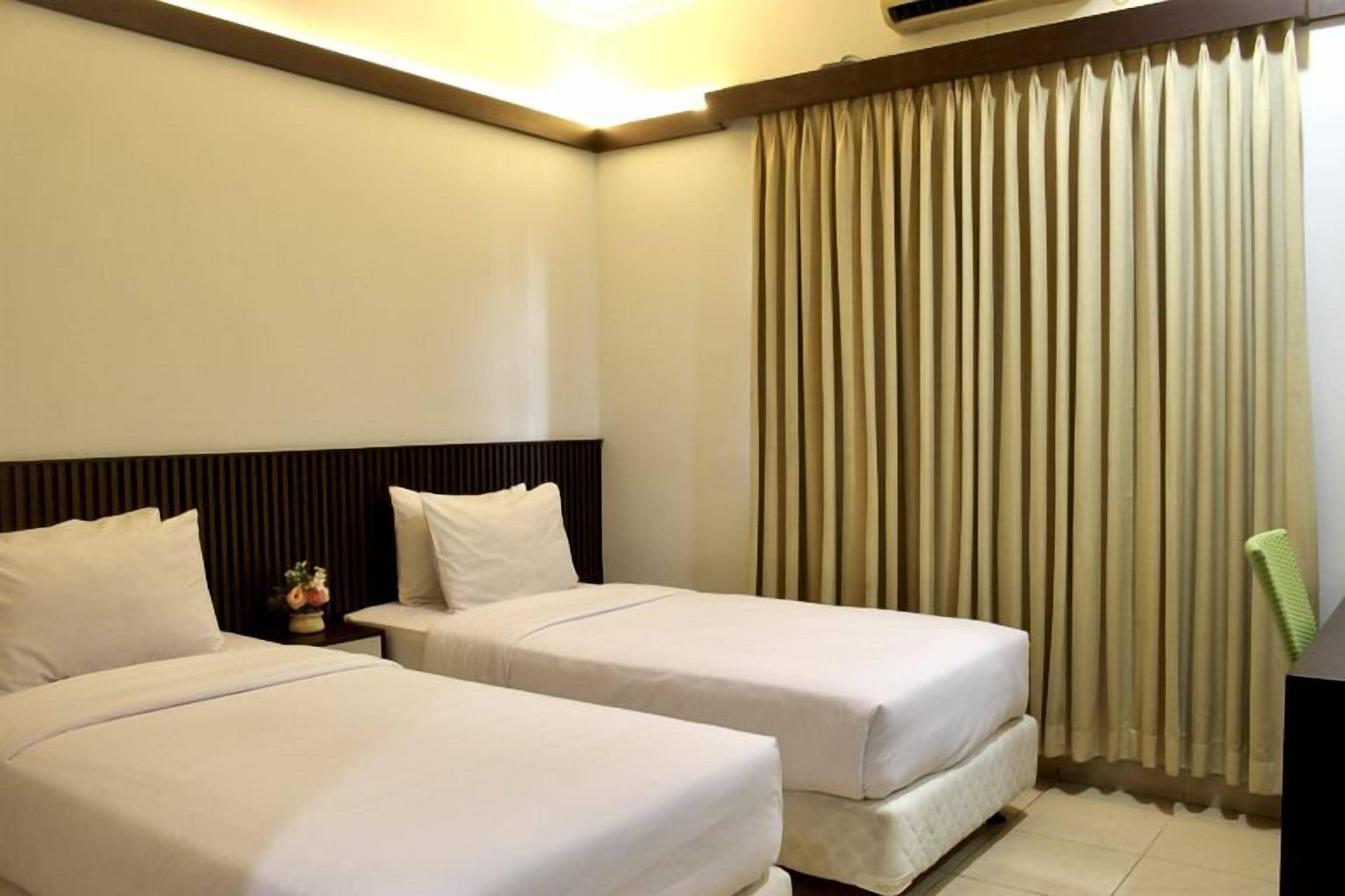 A hotel room with two beds, a nightstand, and a large window with curtains.