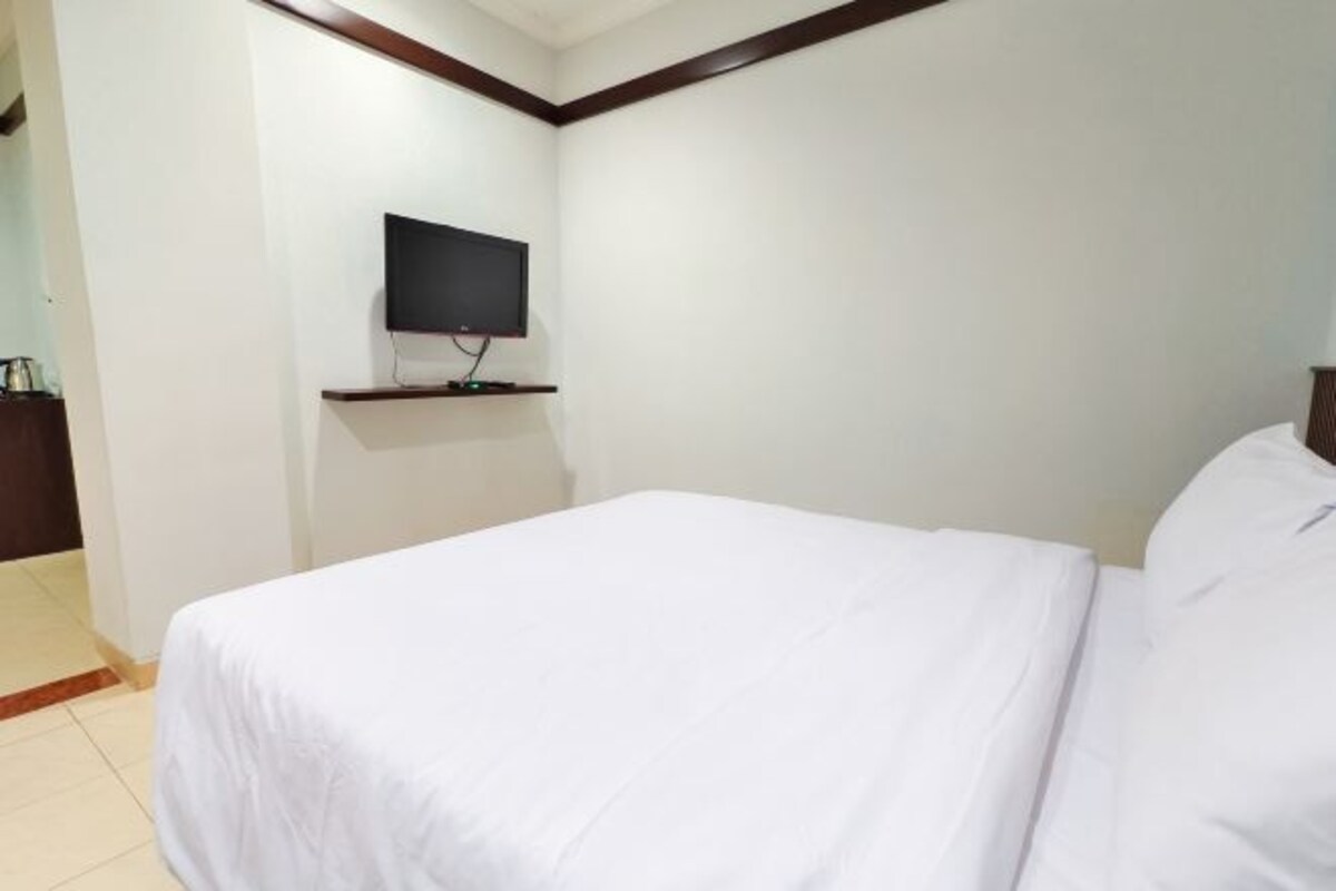 A hotel room with a bed, a flat-screen TV mounted on the wall, and a wooden floor.