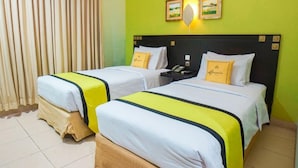A hotel room with two beds, a nightstand, and a wall-mounted lamp. - Hotel Bumi Siliwangi by My Hospitality (Sukasari)