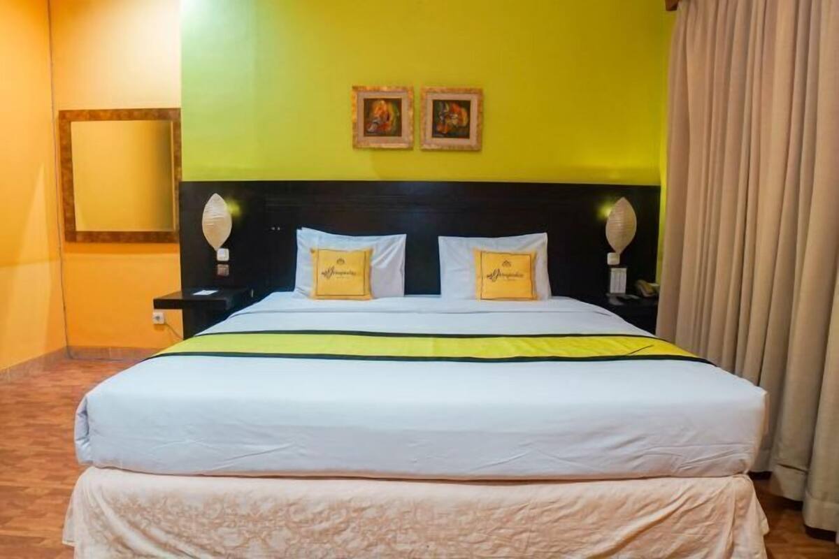 A double bed with a white and yellow bedspread, two bedside tables with lamps, a mirror on the wall, and two framed pictures above the bed.