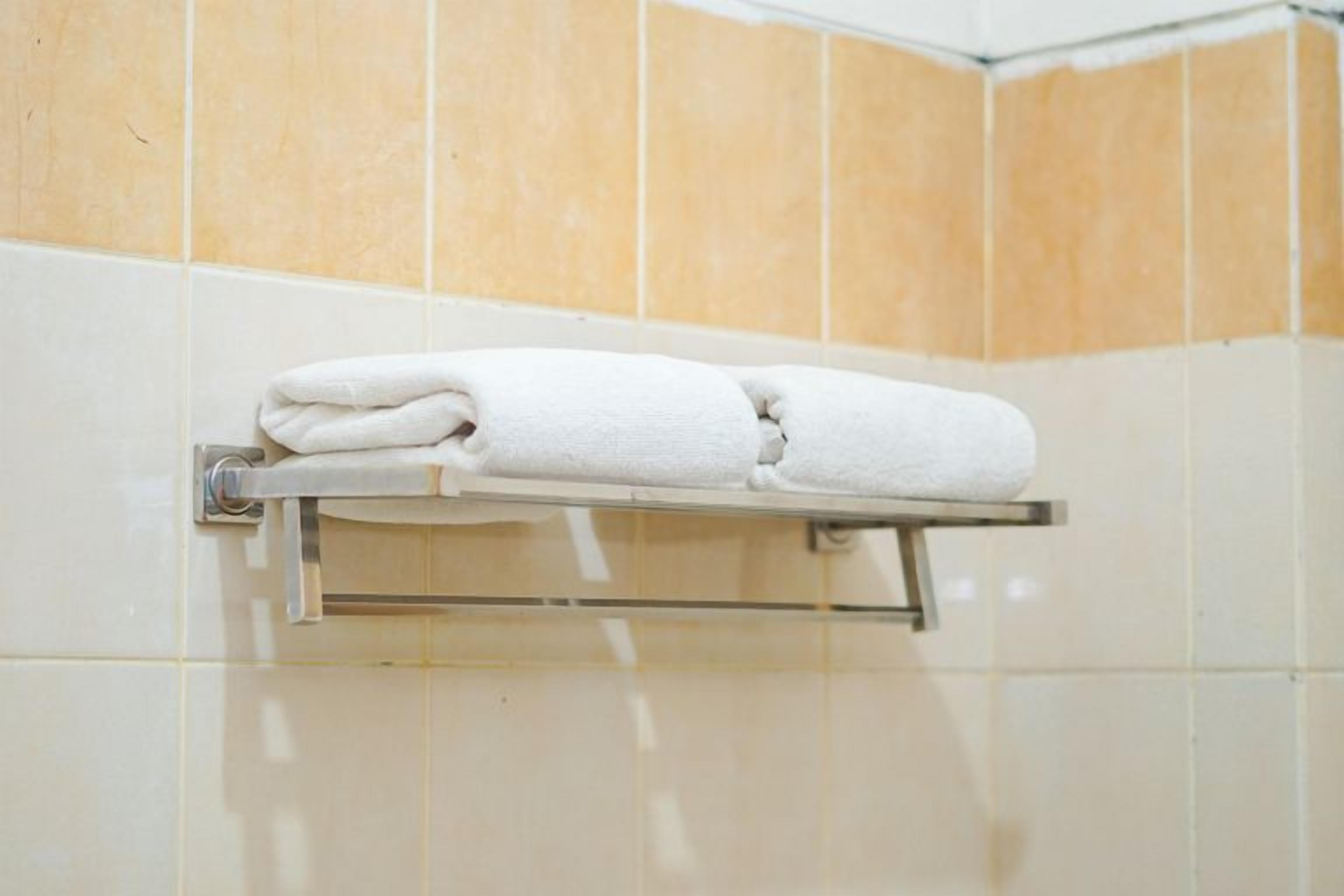 A white towel folded and placed on a metal towel rack in a bathroom with beige tiled walls.