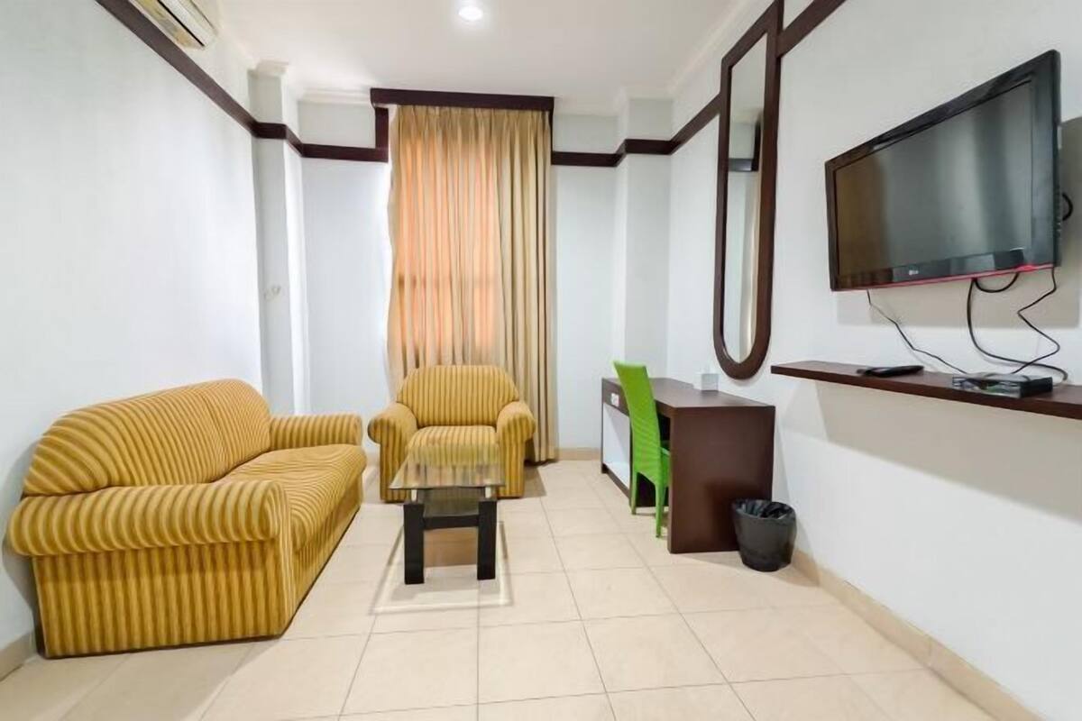 A living room with a sofa, armchair, coffee table, and a TV mounted on the wall.