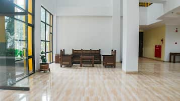 Um hall amplo com piso de mármore polido, área de estar central com bancos e grandes janelas que permitem entrada de luz natural.