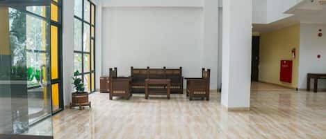 A spacious lobby with a polished marble floor, a central seating area with benches, and large windows allowing natural light.
