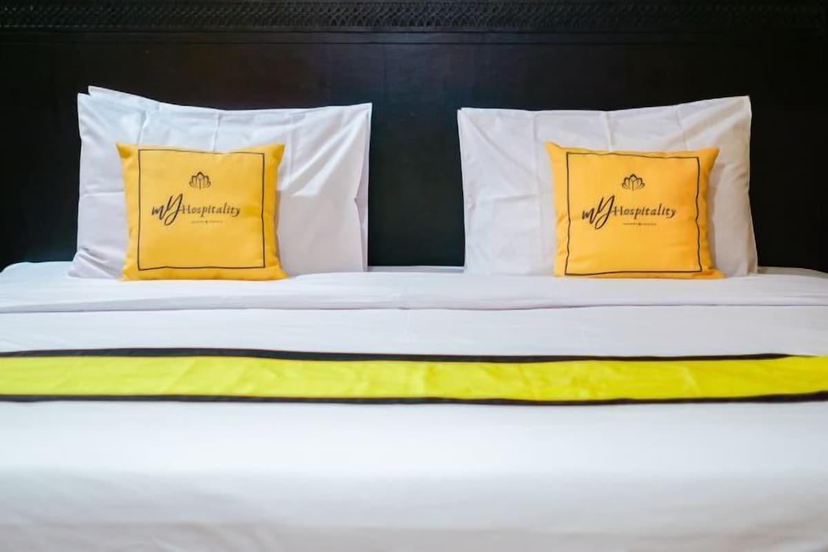 A hotel room with two beds, each with a white mattress and a yellow pillow featuring the hotel's logo.