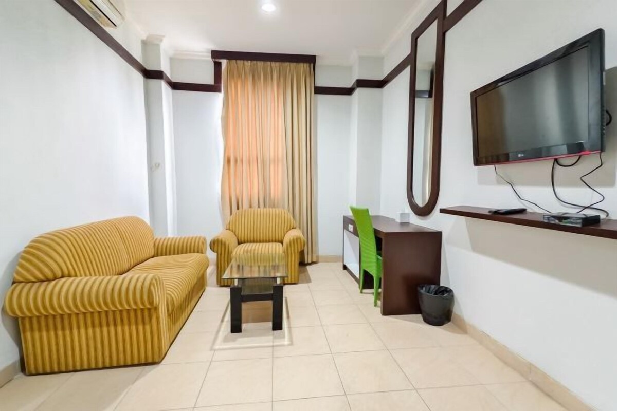 A living room with a sofa, armchair, coffee table, and a TV mounted on the wall.