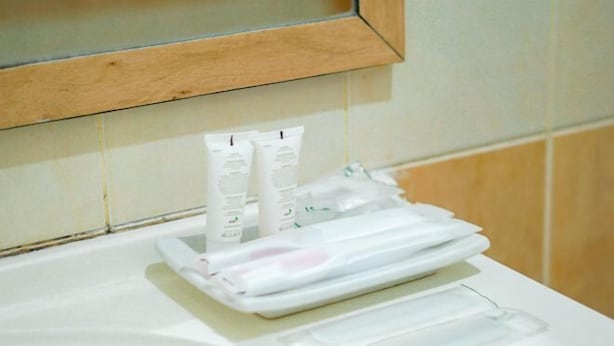 A bathroom with a white sink, a mirror above it, and a towel rack with folded towels and toiletries. - Hotel Bumi Siliwangi by My Hospitality (Sukasari)