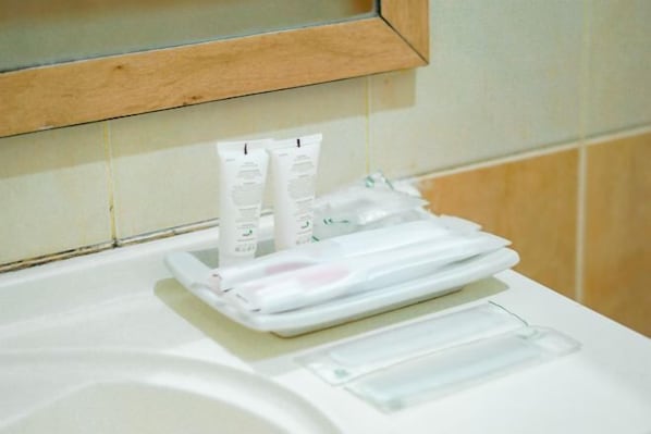 A bathroom with a white sink, a mirror above it, and a towel rack with folded towels and toiletries. - Hotel Bumi Siliwangi by My Hospitality (Sukasari)