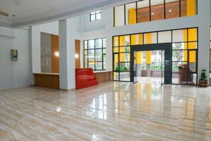 A spacious lobby with a polished floor, a reception desk, and a large window with yellow-tinted glass panels. - Hotel Bumi Siliwangi by My Hospitality (Sukasari)