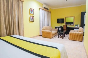 Una habitación de hotel con cama, dos sillones, un escritorio, televisor y espejo.