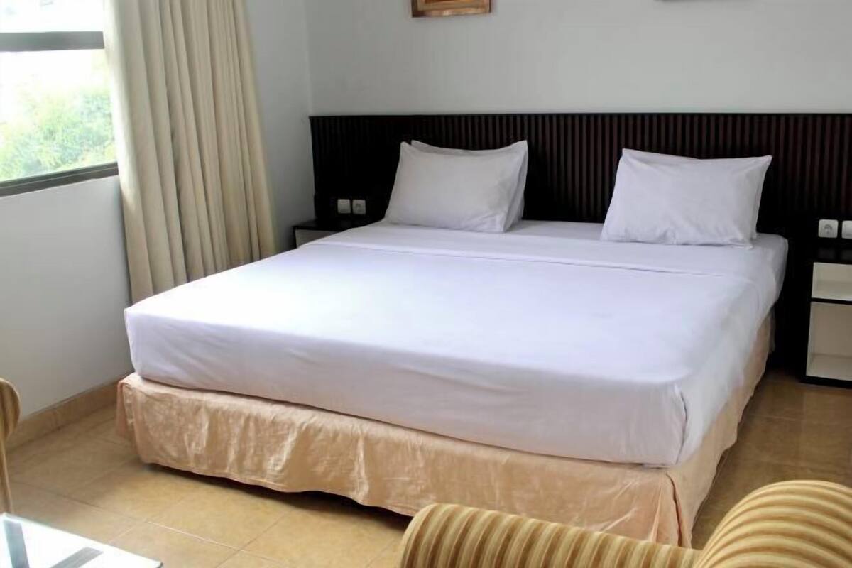 A hotel room with a large bed, a nightstand, a chair, and a window with curtains.